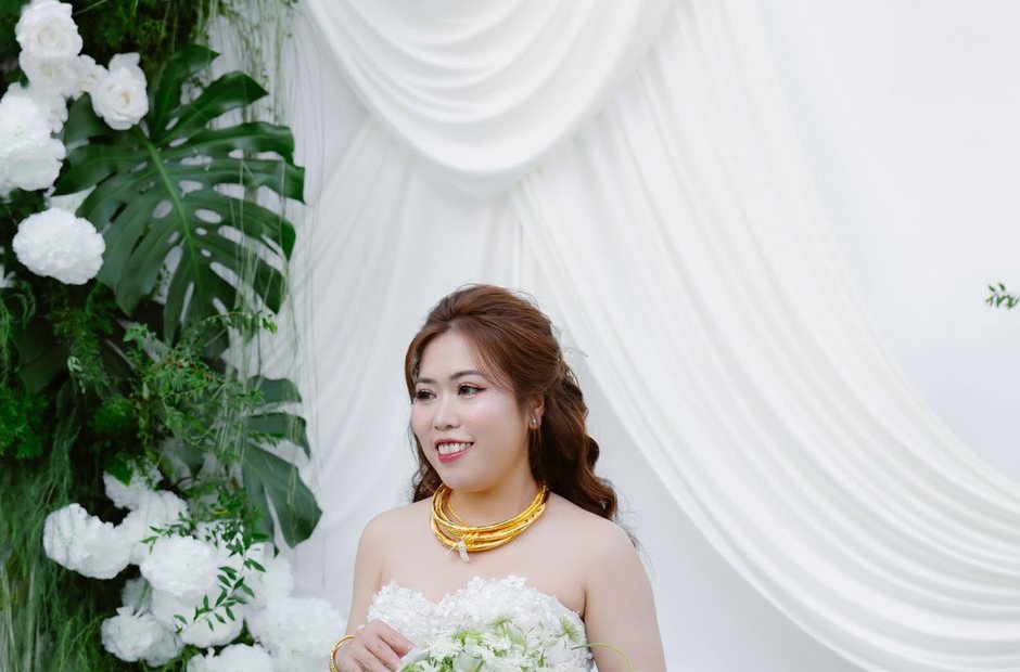 Cô dâu trang điểm tone hồng đứng trước phông hoa trắng