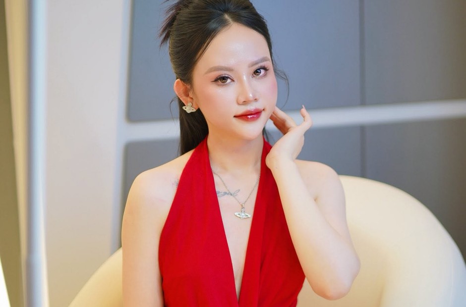 Khách nữ mặc đầm đỏ cổ yếm, tóc buộc cao, ngồi trên ghế bành màu kem