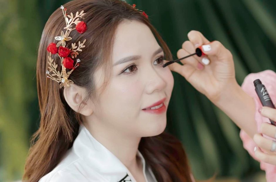 Thợ chuốt mi cho khách mặc áo choàng Kiều Min, tóc cài hoa đỏ