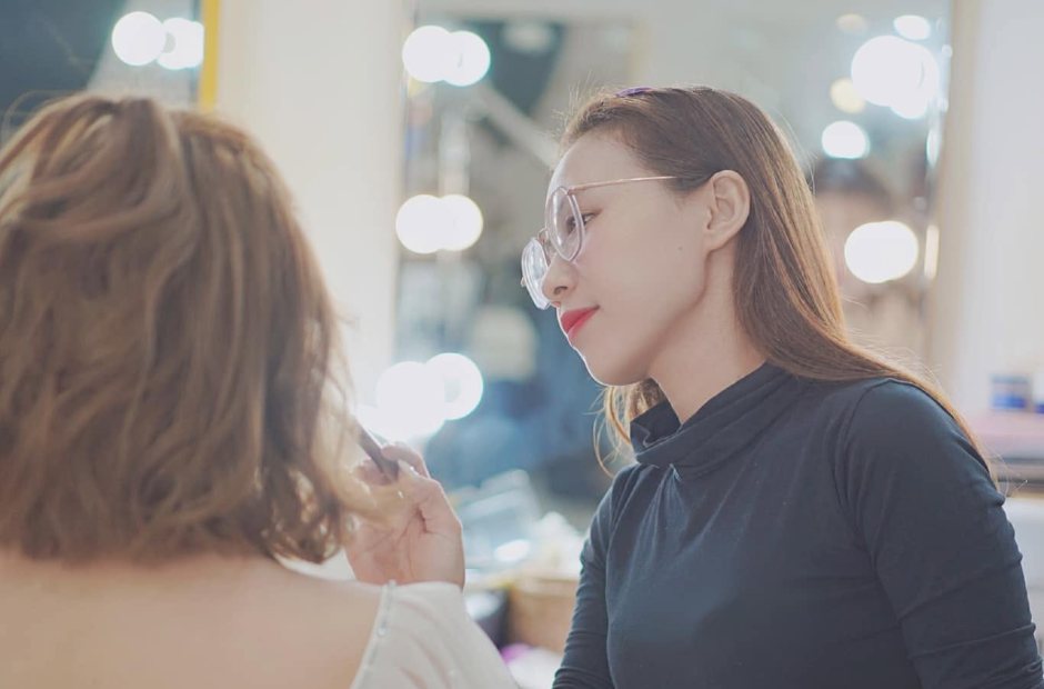 Thợ trang điểm cho khách dưới dàn đèn gương studio