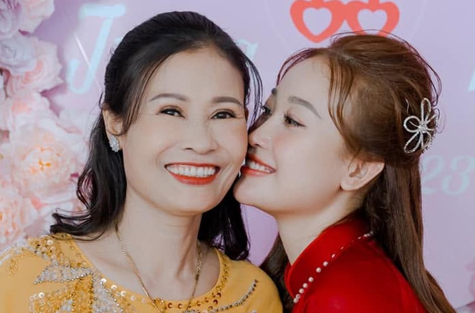 Trang điểm mẹ cô dâu mặc áo dài vàng đứng cạnh con gái áo dài đỏ trước phông cưới