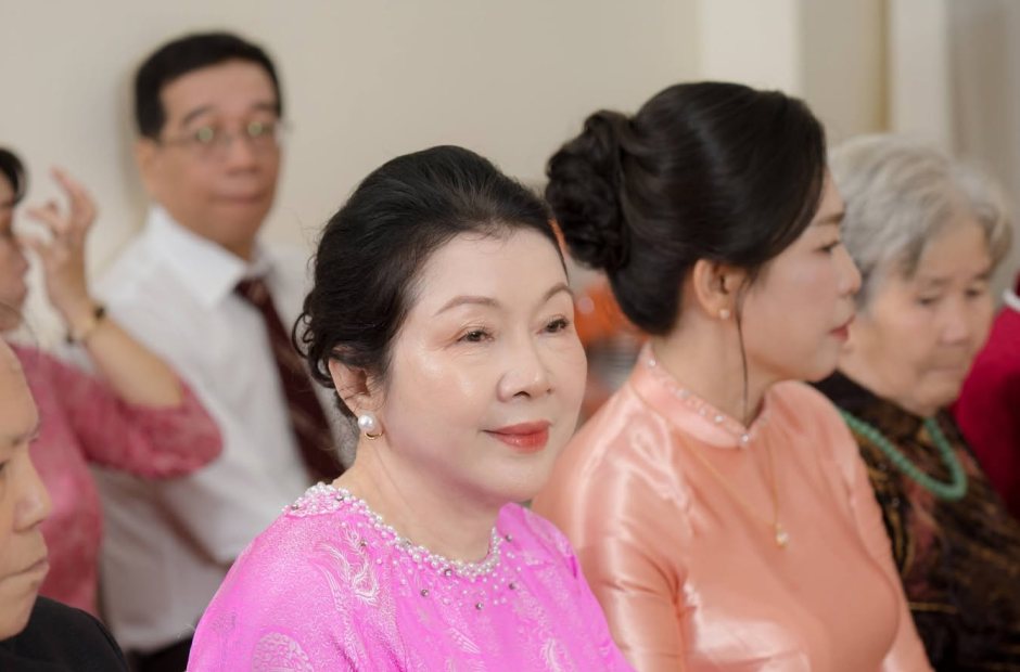 Trang điểm bà sui áo dài hồng ngồi bàn tiệc cưới cùng họ hàng