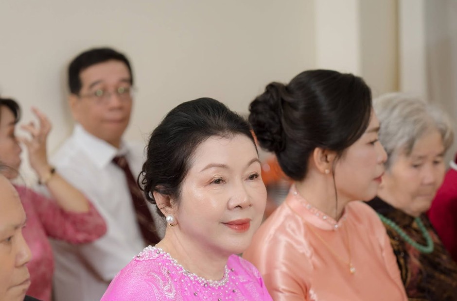Hai người phụ nữ mặc áo dài hồng, tóc búi gọn, ngồi tại bàn tiệc