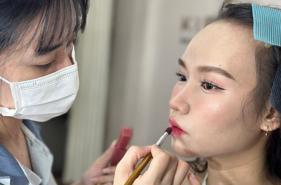 Chuyên viên makeup dùng cọ tán son môi cho khách trước gương có đèn tròn