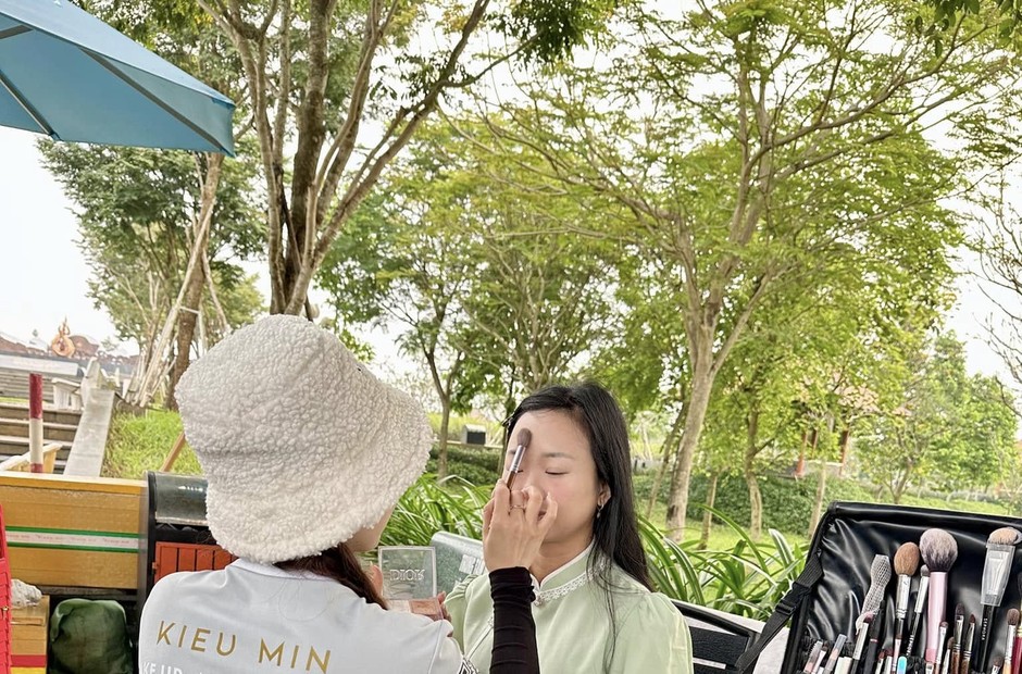 Thợ đội nón trang điểm cho khách ngoài trời, cốp đồ nghề mở sẵn nhiều cọ bên cạnh