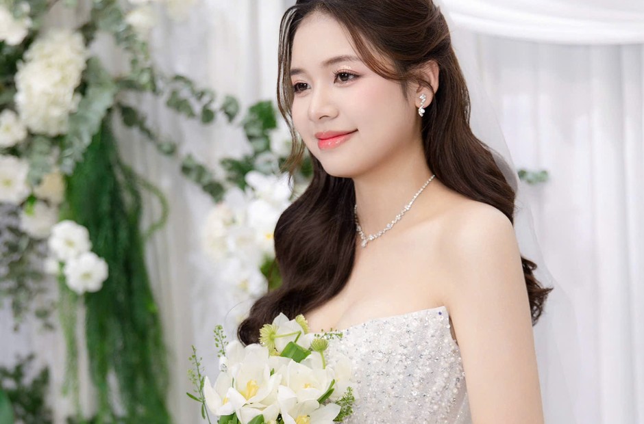 Cô dâu cầm hoa với lớp trang điểm nhẹ trước phông hoa